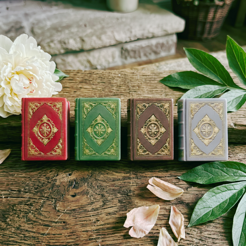 Four Dorians Diaries book bar soap in red, green, brown, and gray on a wooden surface with flowers and leaves.