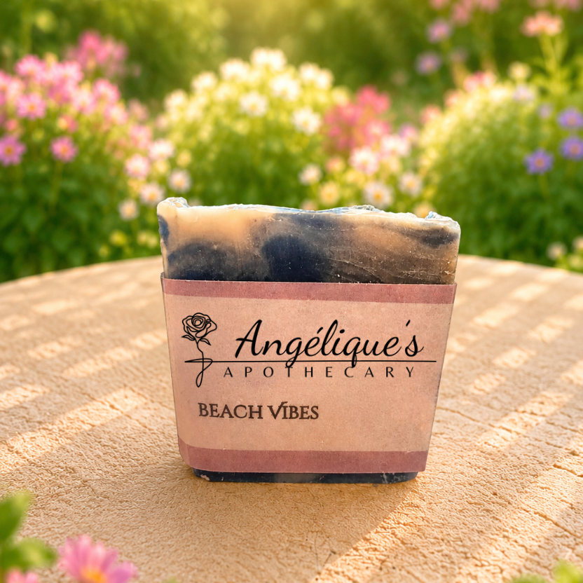 Beach Vibes tallow bar of soap with 'Angélique's Apothecary' packaging on a wooden surface with flowers in the background