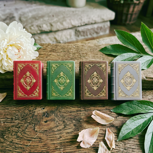 Four Dorians Diaries book bar soap in red, green, brown, and gray on a wooden surface with flowers and leaves.