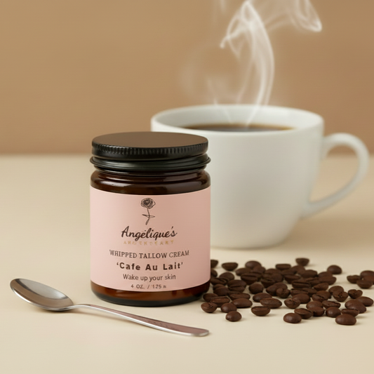 Jar of Angelique's whipped tallow cream labeled 'Cafe Au Lait' with a steaming cup of coffee and coffee beans on a beige background.